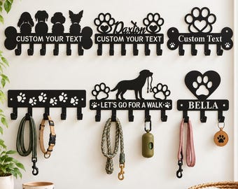 Può includere: Sei supporti da parete in metallo nero per guinzagli e accessori con vari design tra cui sagome di cani, impronte di zampe e forme a cuore. Alcuni riportano testi come CUSTOM YOUR TEXT, Daxton, LET'S GO FOR A WALK e BELLA con ganci.