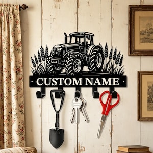May include: Black metal key holder featuring a tractor design with wheat stalks. The key holder has hooks for keys and other items, with the text "CUSTOM NAME" across the front. A small shovel, keys, and scissors hang from the hooks.