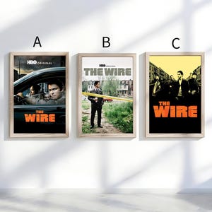 Pode incluir: Três cartazes emoldurados da série da HBO "The Wire". Cada cartaz tem uma moldura de madeira. O primeiro cartaz mostra o interior de um carro com atores. O segundo mostra um homem com fita de precaução. O terceiro tem um fundo amarelo.
