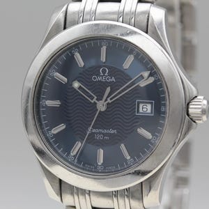 May include: Silver Omega Seamaster wristwatch with a dark blue dial. The watch has silver hands and markers, a date window at 3 o'clock, and a stainless steel bracelet. The dial reads "Omega Seamaster 120 m".