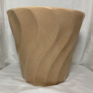 Könnte beinhalten: Beige Keramik-Blumentopf mit strukturiertem, wirbelndem Design. Der Topf hat eine breite, offene Oberseite und einen sich verjüngenden Boden. Die Oberfläche ist mit kleinen, dunkelbraunen Punkten besprenkelt. Die Gesamtform erinnert an eine stilisierte Vase.
