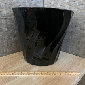 May include: A glossy black planter with a spiraling, fluted design. A wooden ruler is positioned in front of the planter, showing it measures approximately 11 inches in width at the top rim and stands about 9 inches tall from the base.