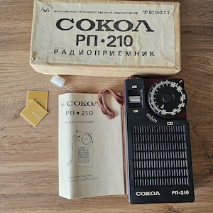 May include: A vintage Sokol RP-210 radio receiver with its original box and manual. The radio is black and burgundy with a tuning dial and speaker grill. The box and manual have Cyrillic text.