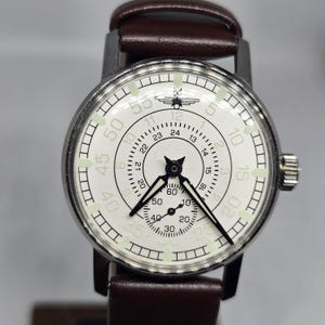 K&ouml;nnte beinhalten: Eine Vintage-Armbanduhr mit wei&szlig;em Zifferblatt, schwarzen Zeigern und einem braunen Lederarmband. Die Uhr hat ein silberfarbenes Geh&auml;use und verf&uuml;gt &uuml;ber mehrere Zifferbl&auml;tter und Markierungen zur Zeitmessung. Das Zifferblatt enth&auml;lt die Zahlen 5, 10, 15, 20, 30, 40, 50 und 55.