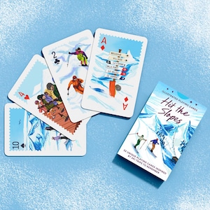 May include: A deck of illustrated playing cards titled Hit the Slopes with a box showing skiers on a mountain. Four cards are fanned out, displaying a 10 of spades, 4 of hearts, 2 of clubs, and an ace of diamonds featuring a ski resort signpost.