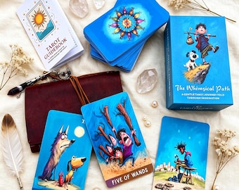 Könnte beinhalten: Ein Tarotkartendeck mit dem Titel The Whimsical Path, bestehend aus einer blauen Schachtel, einem Begleitbuch und drei illustrierten Karten mit den Titeln The Moon, Five of Wands und Eight of Pentacles, ergänzt durch einen braunen Lederbeutel.