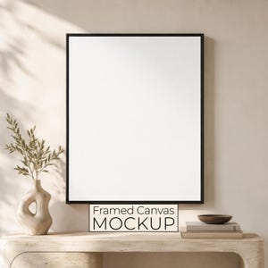 Peut inclure: Une toile blanche vierge rectangulaire verticale encadrée par un cadre noir fin. Sous le cadre, un petit panneau rectangulaire affiche le texte noir Framed Canvas MOCKUP. La composition est centrée et présente une esthétique épurée.