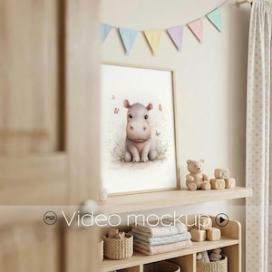 May include: A framed watercolour print of a baby hippo, with butterflies, in a light wood frame. Pastel pennants hang above. A teddy bear and wooden blocks are on a shelf below. The scene is set in a nursery.