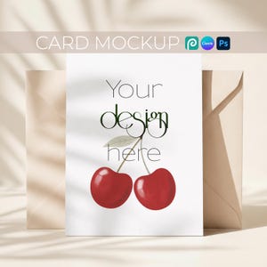 May include: A white card with the text "Your design here" and a cherry illustration, placed in front of a beige envelope. The words "CARD MOCKUP" are at the top. The cherry illustration features two red cherries.