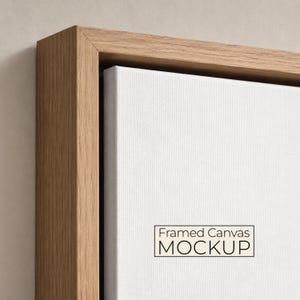 Puede incluir: Un lienzo blanco en blanco colocado dentro de un marco flotante de madera marrón claro. La superficie del lienzo es lisa y texturizada, con el texto negro Framed Canvas MOCKUP impreso en un recuadro rectangular en la parte inferior derecha.