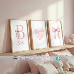 Peut inclure: Trois impressions encadrées avec des cadres en bois clair. Les impressions présentent un « B » rose avec un nœud, un cœur fait de petits cœurs et un nœud rose. Le mot « Bella » est écrit sous la lettre « B ». Les impressions sont exposées sur une étagère.