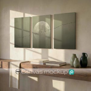 Puede incluir: Un tríptico de lienzo que representa una luna llena y pájaros en vuelo sobre un fondo verde apagado. La obra de arte se exhibe sobre una estantería de madera con libros, jarrones y un paño drapeado. El texto "Canvas mockup" es visible.