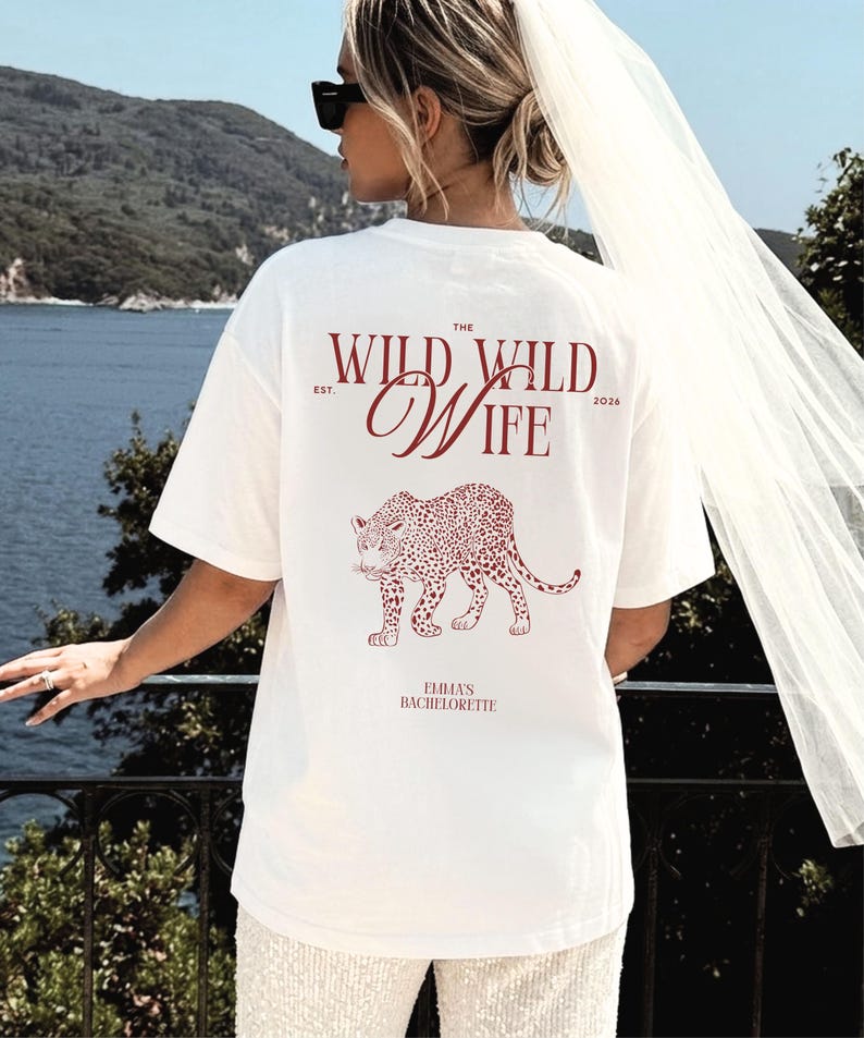 Puede incluir: Camiseta blanca con un dise&ntilde;o de leopardo burdeos y el texto "The Wild Wife" y "Emma's Bachelorette". La camiseta es de corte holgado.