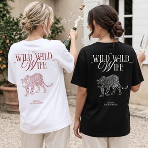 Puede incluir: Dos camisetas, una blanca y otra negra, con un dise&ntilde;o de leopardo y el texto "The Wild Wild Wife" y "Emma's Bachelorette". La camiseta blanca tiene texto burdeos, la camiseta negra tiene texto blanco.