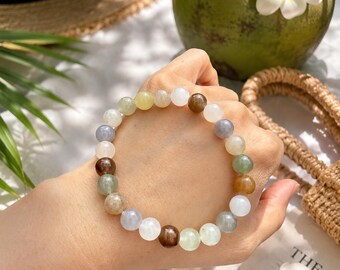 May include: A stretch bracelet composed of smooth, round beads in a variety of translucent and opaque colors, including shades of white, brown, green, gray, and yellow. The beads are arranged in a circular pattern to form a single strand accessory.