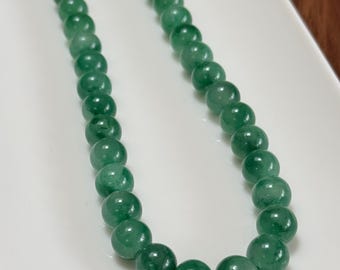 May include: A necklace featuring a strand of round, polished green beads. The beads are strung together with a silver-colored clasp. The necklace is displayed on a white surface.