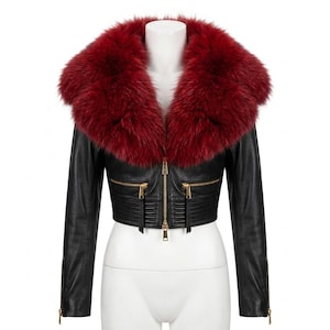 May include: A cropped black leather jacket featuring a large, plush deep red faux fur collar. The jacket includes a central gold-tone zipper, two horizontal zippered pockets on the chest, ribbed detailing at the waist, and gold-tone zippered cuffs.
