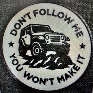 May include: A round, off-white emblem with the text "DON'T FOLLOW ME YOU WON'T MAKE IT" encircling a black Jeep SUV graphic. Two small stars flank the Jeep. The design is embossed.