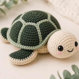 Könnte beinhalten: Eine handgefertigte Häkelschildkröte in Grün und Creme. Die Schildkröte hat einen dunkelgrünen Panzer mit hellgrünen Akzenten, cremefarbene Flossen und Kopf sowie ein lächelndes Gesicht mit schwarzen Augen und rosa Wangen. Ein weiches Spielzeug.