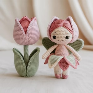 May include: A crocheted fairy doll with a flower-shaped headpiece, wings, and a petal skirt, next to a crocheted tulip. The doll is pink, white, and green. The tulip is pink and green.