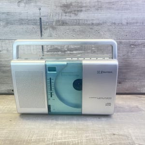 May include: Silver Emerson compact disc player and AM/FM radio with a handle and antenna. The CD player has a clear blue cover. The radio dial is visible on the left side of the unit.