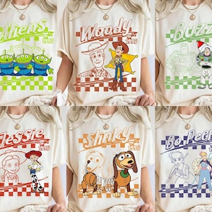 May include: Cream-colored t-shirts featuring various Toy Story characters: Aliens, Woody, Buzz, Jessie, Slinky, and Bo Peep. Each design includes the character's name and the year 1995, set against a checkered background. The graphics are in shades of green, brown, orange, and blue.