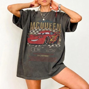 Puede incluir: Camiseta gris oscuro con un gr&aacute;fico de Rayo McQueen de la pel&iacute;cula Cars. El dise&ntilde;o incluye el texto "Lightning McQueen" y "95" en un coche de carreras rojo. La camiseta tambi&eacute;n tiene el texto "I'm Lightning!"
