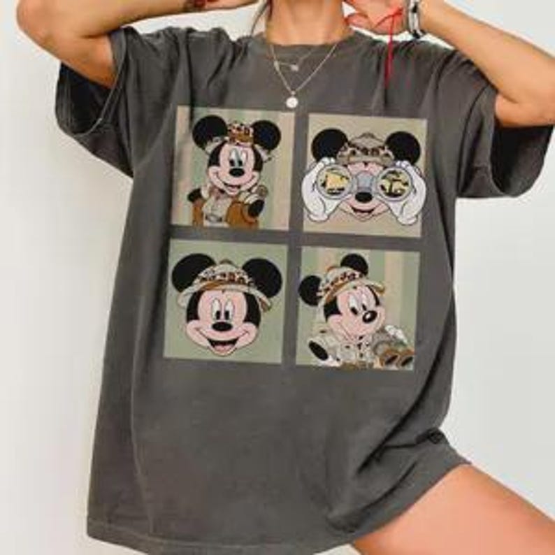 May include: Dark gray t-shirt featuring four panels with Mickey Mouse in safari attire. Each panel shows a different pose of Mickey, wearing a safari hat and holding binoculars. The shirt has a slightly faded, vintage look.