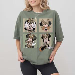 May include: An olive green t-shirt featuring four square images of Minnie Mouse with leopard print bows and accessories. The shirt has a relaxed fit and short sleeves. The design includes sunglasses and peace signs.