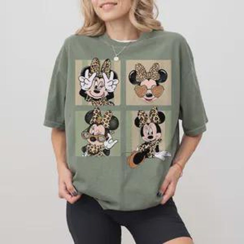 May include: An olive green t-shirt featuring four square images of Minnie Mouse with leopard print bows and accessories. The shirt has a relaxed fit and short sleeves. The design includes sunglasses and peace signs.