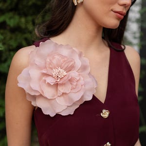 Puede incluir: Vestido burdeos sin mangas con botones dorados y cinturón a juego. Una gran flor rosa claro adorna el hombro. Pendientes dorados con pequeños cristales. Adecuado para eventos formales.