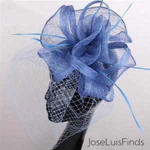 Könnte beinhalten: Ein periwinkelfarbener blauer Fascinator mit einem geschichteten, strukturierten Design. Der Kopfschmuck hat einen Netzschleier und ist mit zarten, hellblauen Federn verziert. Der Text "JoseLuisFinds" ist unten rechts sichtbar.