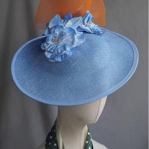 May include: A sky blue hat with a wide brim, decorated with blue fabric flowers and an orange mesh detail. The hat is displayed on a mannequin head, highlighting its elegant design.