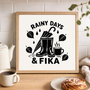 Könnte beinhalten: Ein quadratischer Holzrahmen mit einem weißen Druck, der schwarze Grafiken von Gummistiefeln, einem Regenschirm, fallenden Blättern und einer dampfenden Tasse zeigt. Der Text RAINY DAYS & FIKA steht in fetten schwarzen Buchstaben auf dem Bild.