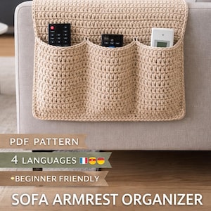 May include: Beige crochet sofa armrest organizer with three pockets, holding remote controls. The organizer is attached to a light-colored sofa arm. The image includes text that says "PDF Pattern", "4 Languages", and "Beginner Friendly".