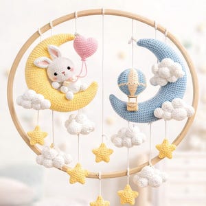Puede incluir: Móvil de guardería hecho a mano con una luna amarilla de ganchillo, un conejito blanco y un globo de corazón rosa. Incluye una luna azul, un globo aerostático, nubes blancas y estrellas amarillas. El texto "Nursery Mobile" y "CROCHET PATTERN PDF Download" son visibles.