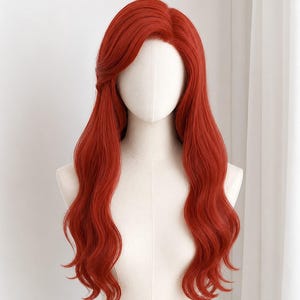 Könnte beinhalten: Eine lange, leuchtend rote Perücke mit Seitenscheitel und lockeren, fließenden Wellen. Das Haar hat einen tiefen, gesättigten kupferroten Farbton und ist mit weichen, voluminösen Locken gestylt, die über die Schultern des weißen Schaufensterkopfes fallen.