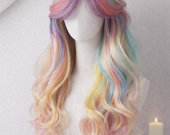 May include: A pastel rainbow wig with long, wavy hair. The wig features shades of pink, yellow, blue, and purple. The wig is styled on a mannequin head, with a candle in a decorative holder in the background.