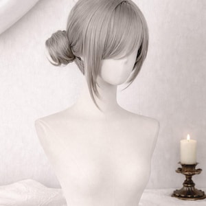May include: A light ash-blonde wig styled with a side-swept fringe and a low bun at the nape of the neck. The hair features a smooth, straight texture with a single loose strand arching over the top, displayed on a plain white mannequin bust.