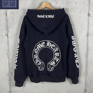 May include: A black hooded sweatshirt featuring white graphic text on the back and sleeves. The back displays a large circular Chrome Hearts logo, while the hood features the text FUCK YOU in a gothic font. The sleeves also include white text.