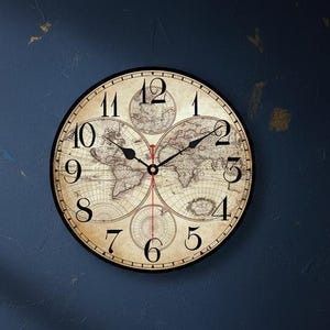 May include: A round wall clock with a world map design. The clock face has black Roman numerals and black hands. The clock is set against a dark blue wall, with a desk and books in the foreground.