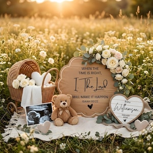 Puede incluir: Una conmovedora escena de anuncio de embarazo. Un cochecito de mimbre con flores blancas y un osito de peluche sobre una manta blanca. Un letrero de madera con el texto "When the time is right, I, The Lord, will make it happen" y un letrero en forma de corazón.
