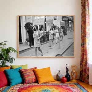 May include: A framed black and white photograph shows a protest from the 1960s. Women in mini skirts march with signs that read "Forever" and "Mini Skirts". A man in uniform stands in the background.