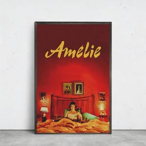 以下が含まれることがあります： 映画「アメリ」の額入りポスター。金色の文字でタイトルが書かれています。ベッドで読書をする女性が描かれており、背景は赤色です。ベッドの両側には額入りの写真とランプが見えます。