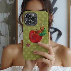 Puede incluir: Una funda de tel&eacute;fono verde con un dise&ntilde;o de manzana roja y oruga de dibujos animados. La funda tiene un patr&oacute;n de lunares y una estrella roja. La funda est&aacute; dise&ntilde;ada para un tel&eacute;fono inteligente.
