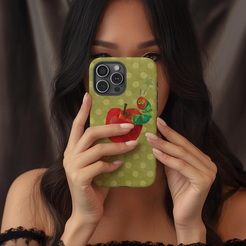 Puede incluir: Funda de tel&eacute;fono verde con una ilustraci&oacute;n de una manzana roja y una oruga verde. La funda tiene un patr&oacute;n de lunares y un recorte para la c&aacute;mara. El dise&ntilde;o est&aacute; inspirado en un libro infantil.