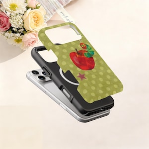 Puede incluir: Una funda de tel&eacute;fono con un patr&oacute;n de lunares verdes y un dise&ntilde;o de manzana roja con una oruga verde. La funda es negra y verde y est&aacute; sobre un tel&eacute;fono plateado.
