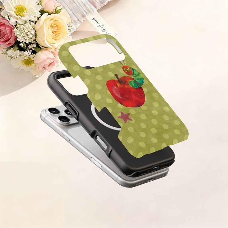 Puede incluir: Una funda de tel&eacute;fono con un patr&oacute;n de lunares verdes y un dise&ntilde;o de manzana roja con una oruga verde. La funda es negra y verde y est&aacute; sobre un tel&eacute;fono plateado.