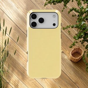 May include: A pale yellow phone case with a black border. The case has a camera cutout with three lenses and a flash. The phone case is on a wooden surface.