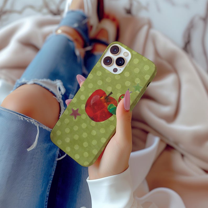 Puede incluir: Una funda de tel&eacute;fono verde con un dise&ntilde;o de lunares y una ilustraci&oacute;n de una manzana roja. Tambi&eacute;n hay una estrella roja en la funda. La funda del tel&eacute;fono la sostiene una persona que lleva vaqueros azules.